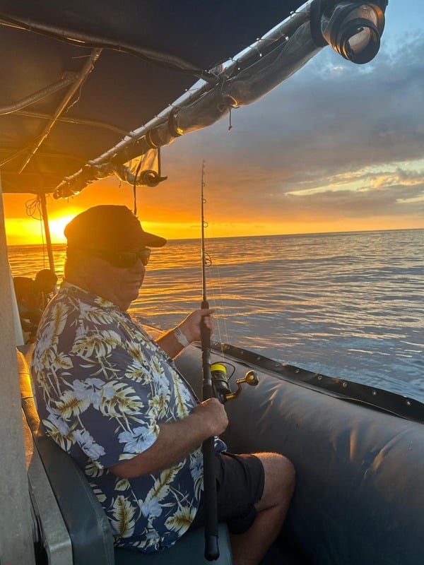 A guest fishing aboard a boat at sunset
